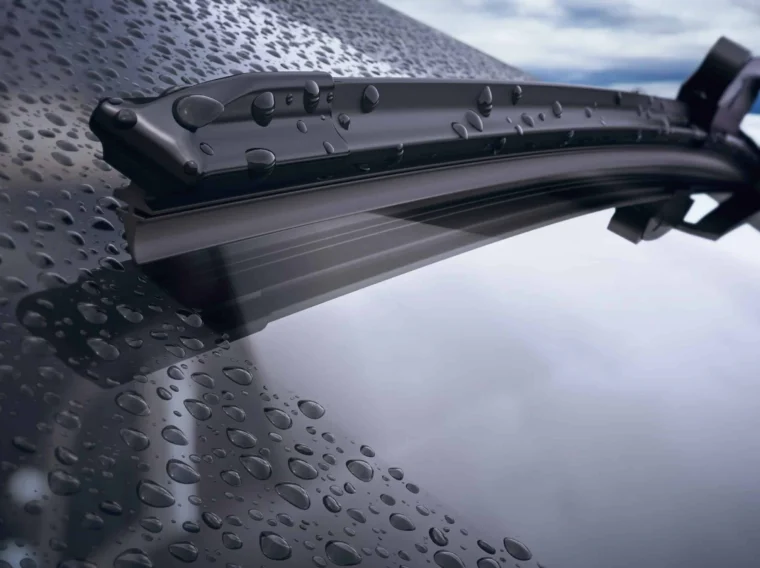 Close-up of windshield wiper blades clearing rainwater droplets from a car windshield.