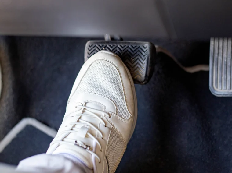 A person wearing a white sneaker presses a car brake pedal, with the accelerator visible nearby—perfect imagery for clutch replacement or cylinder replacement scenarios.