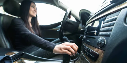 A person sitting in the driver’s seat of a car is holding the steering wheel with one hand and shifting the gear with the other, possibly after a recent clutch replacement.