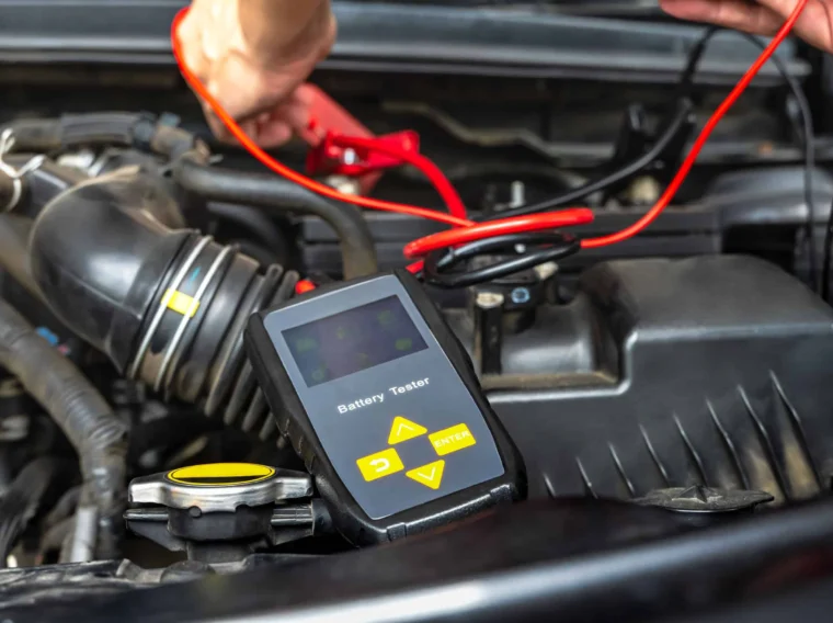 A person uses a digital battery tester to check a car battery under the hood, with red and black testing cables connected—an essential step in quality Battery Services.