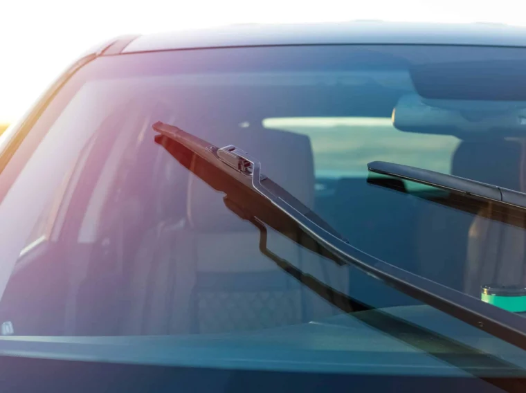 Close-up view of a car windshield with one wiper raised, showing the interior in the background—perfect for illustrating wiper replacement or wiper blade replacement services.