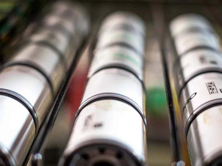 Close-up view of cylindrical metal objects, possibly batteries or industrial components, arranged in parallel rows on a metal rack.