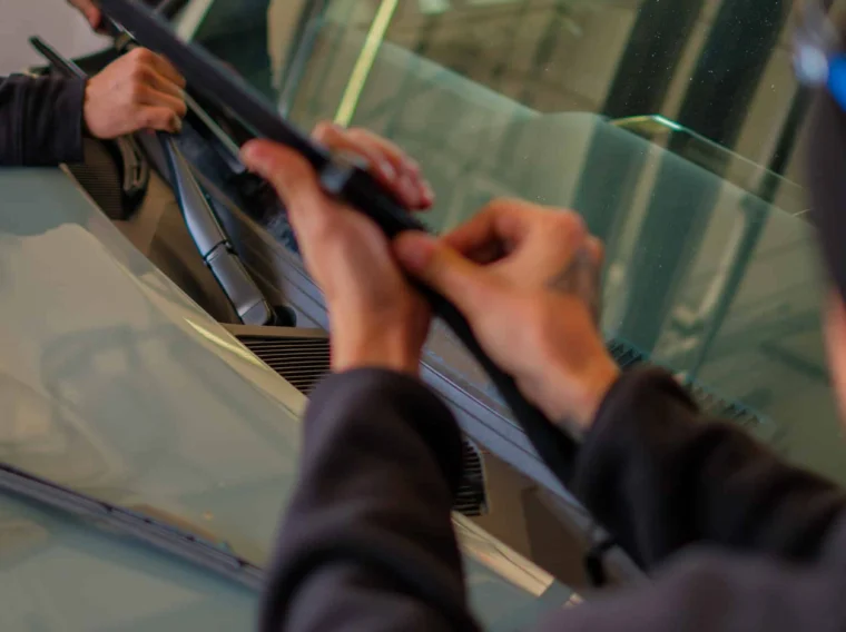 Two people are installing or replacing windshield wiper blades on a car as part of routine maintenance and State Inspection Services.
